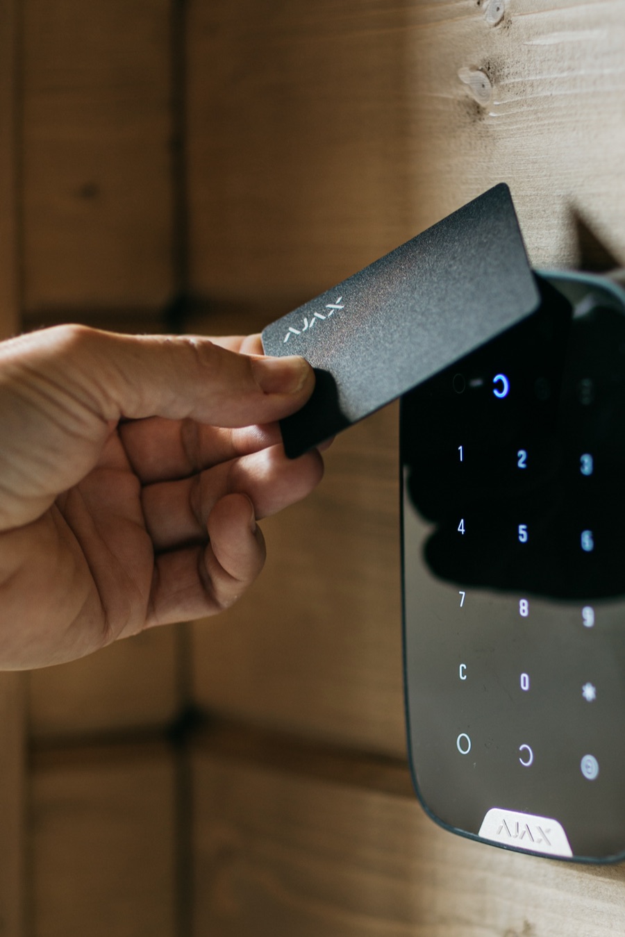 A hand presenting an Ajax key card to a wall-mounted keypad