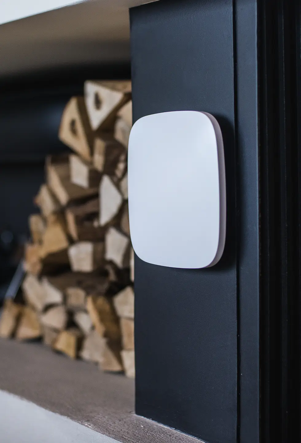 A white Ajax hub mounted on a wall beside a stack of firewood